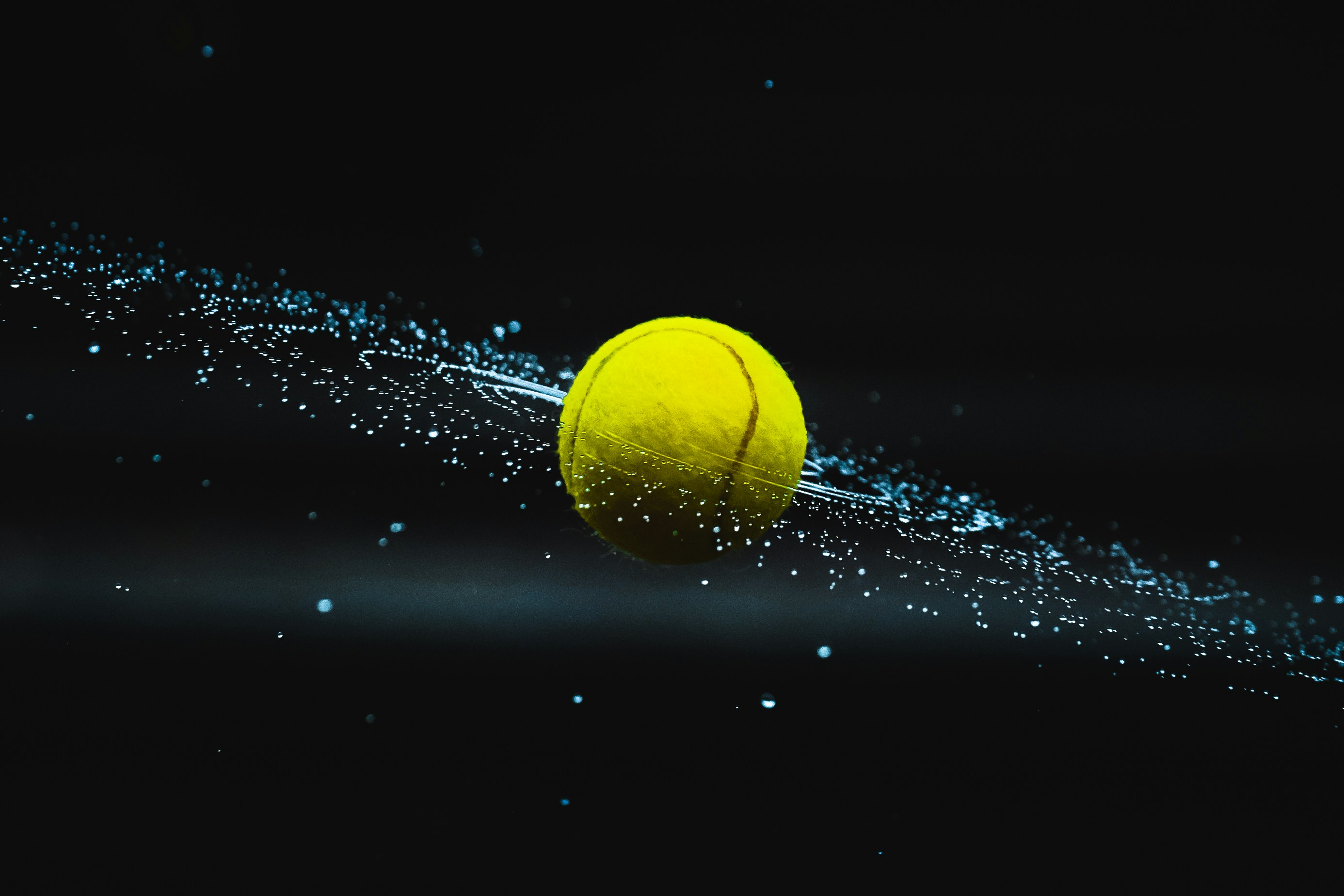 Yellow tennis ball spinning fast with water droplets spraying on black